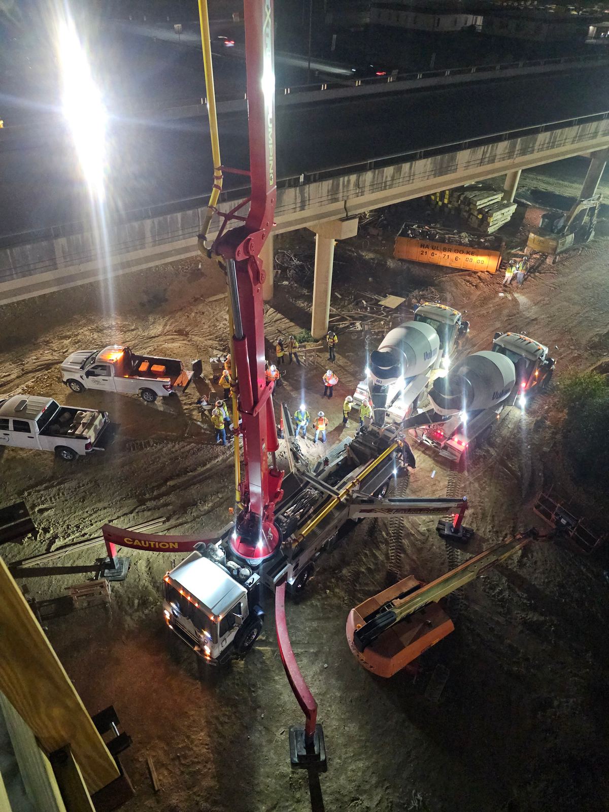 Crane lifting a concrete girder into place at night on a TxDOT bridge project